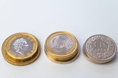 Beyaz yüzeyde Euro, Pound ve Swiss Franc sikkeleri. İsviçre Frangı, Sterlin ve Euro 'nun değeri, döviz kuru eğilimi.