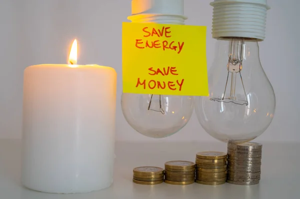 Lit candle, next to two unlit bulbs, and a yellow note with the text 