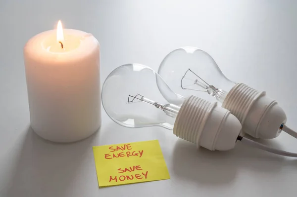Lit candle, next to two unlit bulbs, and a yellow note with the text \