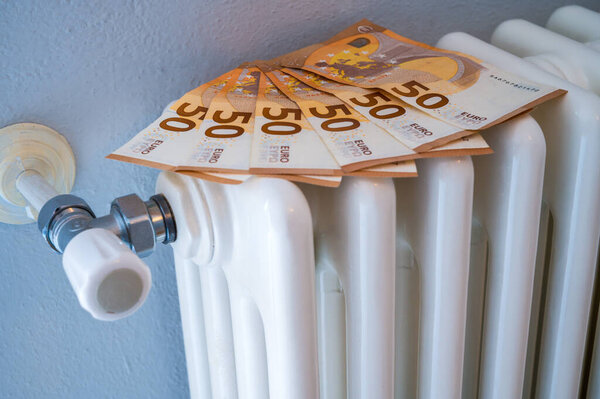 White radiator, with euro banknotes above it. Increase in heating costs and gas tariffs.
