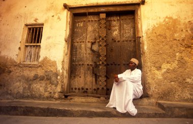 Tanzanya 'nın Zanzibar Adası' ndaki Taş Kasaba 'nın geleneksel ahşap kapısındaki yerel bir adam. Tanzanya, Zanzibar, Taş Şehir, Ekim 2004