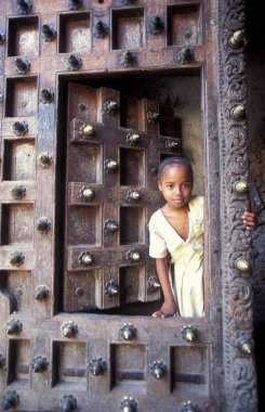 Tanzanya 'nın Zanzibar Adası' ndaki Taş Kasaba 'nın geleneksel ahşap kapısındaki yerel bir adam. Tanzanya, Zanzibar, Taş Şehir, Ekim 2004