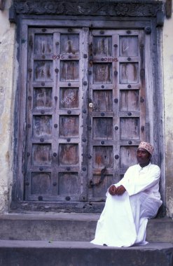 Tanzanya 'nın Zanzibar Adası' ndaki Taş Kasaba 'nın geleneksel ahşap kapısındaki yerel bir adam. Tanzanya, Zanzibar, Taş Şehir, Ekim 2004