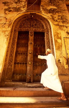 Tanzanya 'nın Zanzibar Adası' ndaki Taş Kasaba 'nın geleneksel ahşap kapısındaki yerel bir adam. Tanzanya, Zanzibar, Taş Şehir, Ekim 2004