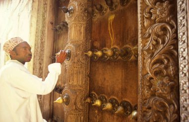 Tanzanya 'nın Zanzibar Adası' ndaki Taş Kasaba 'nın geleneksel ahşap kapısındaki yerel bir adam. Tanzanya, Zanzibar, Taş Şehir, Ekim 2004