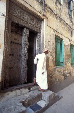 Tanzanya 'nın Zanzibar Adası' ndaki Taş Kasaba 'nın geleneksel ahşap kapısındaki yerel bir adam. Tanzanya, Zanzibar, Taş Şehir, Ekim 2004