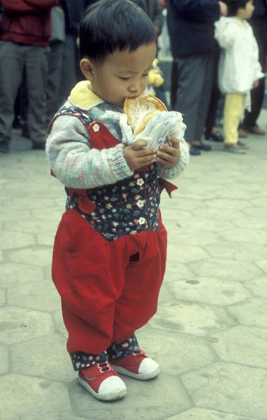 Çin 'in Pekin şehir merkezinde elinde hamburgerle Çinli bir çocuk. Çin, Pekin, Ekim 1997