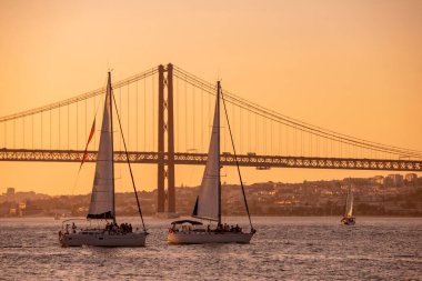 Sailboat with the Ponte 25 de Abril or 25the April Bridge at the Rio Tejo near the City of Lisbon in Portugal.  Portugal, Lisbon, October, 2021