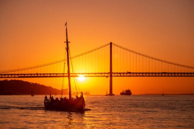 Sailboat with the Ponte 25 de Abril or 25the April Bridge at the Rio Tejo near the City of Lisbon in Portugal.  Portugal, Lisbon, October, 2021