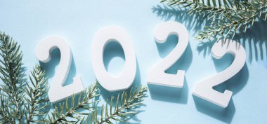 - Mutlu yıllar. Beyaz ahşap numaralar 2022, yeşil dallar köknar ağacı, mavi arka planda koni. Tebrik kartı. Üst manzara, düz yatış. Pankart