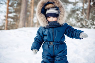 Karlı ladin ormanındaki bir çocuğun portresi. Küçük çocuk kışın dışarıda eğleniyor. Noel tatili. Mavi tulumlu, örgü örüp parkta yürüyen şirin bir çocuk..
