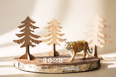 Kaplan heykeli, ahşap köknar ağaçları ve 2022 numara pastel bej arka plandaki doğal ahşap standı. 2022 Çin Yeni Yılı 'nın kaplan sembolü. Tebrik kartı. Ahşap mahsul ve eko tarzı.