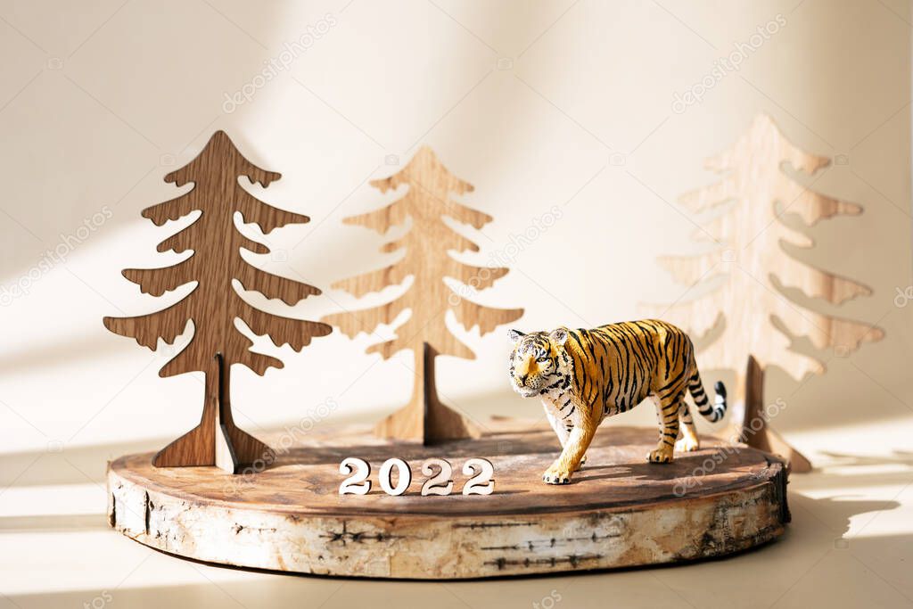 Figurine of tiger, wooden fir trees and numbers 2022 on natural wooden stand on pastel beige background. Tiger symbol of the Chinese new year 2022. Greeting card. Wooden vintage and eco style.