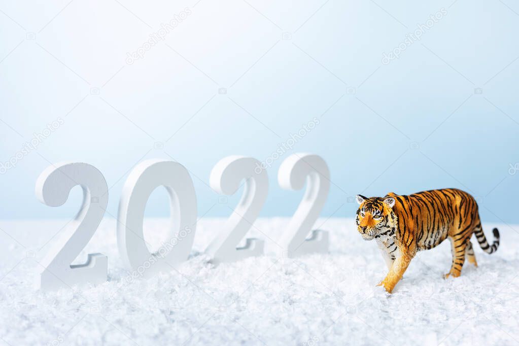 Happy New Year 2022. Decorative white number 2022 and figurine of tiger isolated on blue background. Christmas greeting card.
