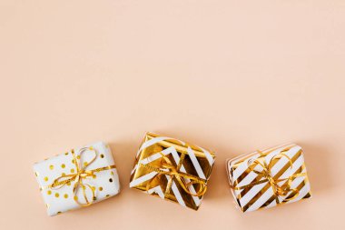 Bej renkli pastel arka planda izole edilmiş altın yaylı beyaz hediye kutuları. Noel ve yeni yıl alışverişi ve satışı. Uzayı kopyala, çerçeve. Pankart. Tatil ve kutlama konsepti