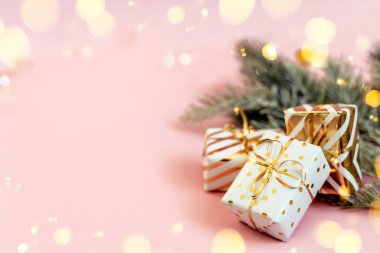 Pastel pembe arka planda karlı köknar dallarıyla altın fiyonklu beyaz hediye kutuları. Noel, yeni yıl, şenlik, tatil, kutlama ya da kışın fotokopi alanı olan arka plan. Online alışveriş ve satış.