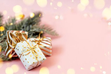 Pastel pembe arka planda karlı köknar dallarıyla altın fiyonklu beyaz hediye kutuları. Noel, yeni yıl, şenlik, tatil, kutlama ya da kışın fotokopi alanı olan arka plan. Online alışveriş ve satış.