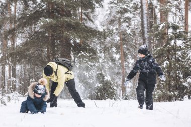 Baba ve oğulları kış ormanında kartopu savaşı yapıyorlar. Dışarıda karda oynayan mutlu çocuklar. Noel tatili, yeni yıl aile tatili. Sıcak giysili kardeşler soğuk günde yürürler.