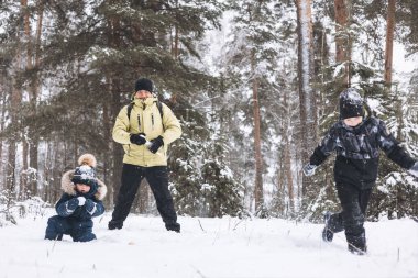 Baba ve oğulları kış ormanında kartopu savaşı yapıyorlar. Dışarıda karda oynayan mutlu çocuklar. Noel tatili, yeni yıl aile tatili. Sıcak giysili kardeşler soğuk günde yürürler.