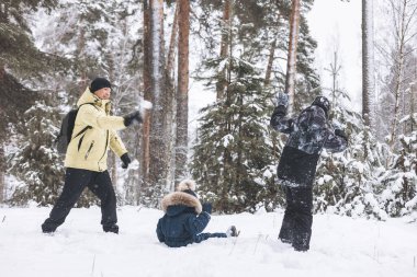 Baba ve oğulları kış ormanında kartopu savaşı yapıyorlar. Dışarıda karda oynayan mutlu çocuklar. Noel tatili, yeni yıl aile tatili. Sıcak giysili kardeşler soğuk günde yürürler.