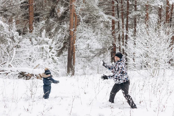 冬の森の中で一緒に雪玉を楽しんでいる父と息子 屋外で雪の中で遊ぶ幸せな子供たち クリスマス休暇 新年の家族の休暇 寒い日に歩く暖かい服の兄弟 — ストック写真