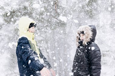 Kış ormanlarında kar yağan mutlu gençler. Çocuklar dışarıda eğleniyor. Kar yağarken karda oynayan neşeli kardeşler. Soğuk havada kış parkında yürüyen gülen çocuklar.