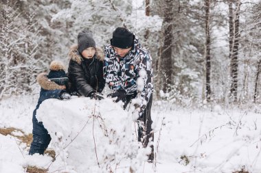 Karlı kış ormanlarında kardan adam için büyük bir kartopu yuvarlayan mutlu baba ve oğullar. Neşeli genç bir adam ve küçük bir çocuk aile yürüyüşünde eğleniyor. Kış zamanı açık hava aktivitesi.