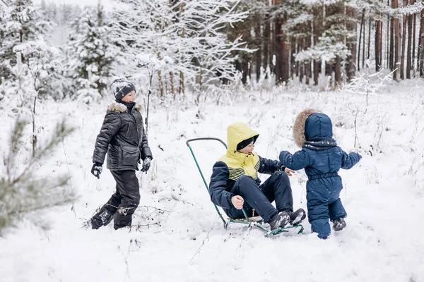 冬の雪の森で寝ている幸せな子供たち 10代の男の子と幼児は楽しい乗馬そりを持っていて 霜の日に遊んでいます 冬の野外活動 暖かい服を着た楽しい兄弟が歩く — ストック写真