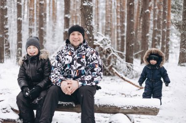Mutlu baba ve küçük oğullar kış karlı ormanında kütüğün üzerinde oturmaktan keyif alıyorlar. Neşeli adam ve genç çocuk dinleniyor. Açık havada arkadaşça olumlu konuşuyorlar.