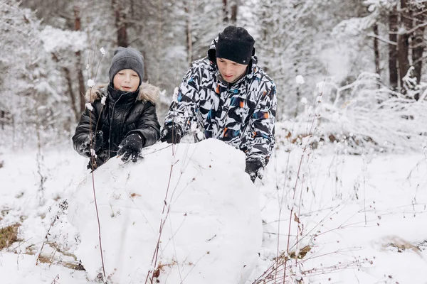雪深い冬の森の中で雪男のために一緒に大きな雪玉を転がす幸せな父と小さな息子 男喜びと10代の男の子が遊んで家族の散歩を楽しんでいます 冬のアクティビティ — ストック写真
