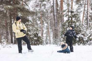 Baba ve oğulları kış ormanında kartopu savaşı yapıyorlar. Dışarıda karda oynayan mutlu çocuklar. Noel tatili, yeni yıl aile tatili. Sıcak giysili kardeşler soğuk günde yürürler.