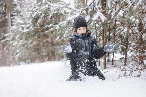 冬の森の雪の上に座って幸せな10代の少年 子供は屋外で楽しんでいます 雪の中で雪の中で遊ぶ楽しい青年 寒い日に冬の公園を歩く笑顔の子供 — ストック写真