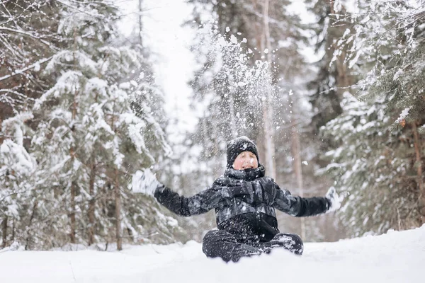 冬の森の雪の上に座って幸せな10代の少年 子供は屋外で楽しんでいます 雪の中で雪の中で遊ぶ楽しい青年 寒い日に冬の公園を歩く笑顔の子供 — ストック写真