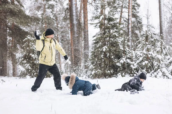 冬の森の中で一緒に雪玉を楽しんでいる父と息子 屋外で雪の中で遊ぶ幸せな子供たち クリスマス休暇 新年の家族の休暇 寒い日に歩く暖かい服の兄弟 — ストック写真