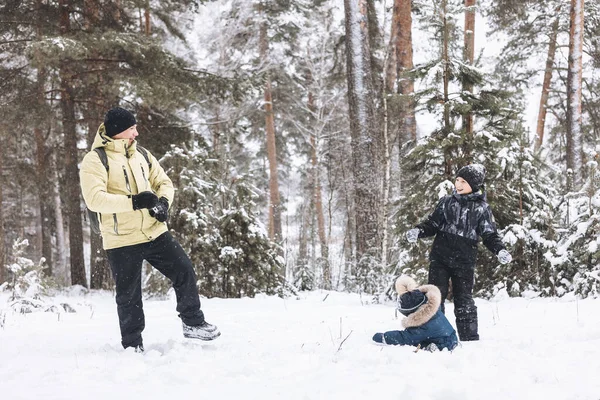 Baba ve oğulları kış ormanında kartopu savaşı yapıyorlar. Dışarıda karda oynayan mutlu çocuklar. Noel tatili, yeni yıl aile tatili. Sıcak giysili kardeşler soğuk günde yürürler.