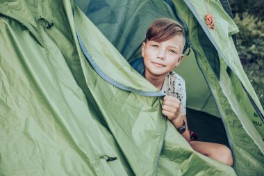 Teenager boy sitting in camping tent. Family weekend outdoor.
