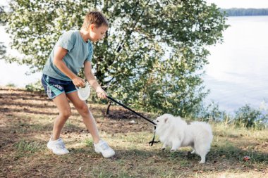 Çocuk dışarıda parkta evcil köpek yavrusuyla oynuyor. Beyaz Pomeranya 'lı köpek yavrusu yazın ormanda köpek gezdirip eğitiyor.