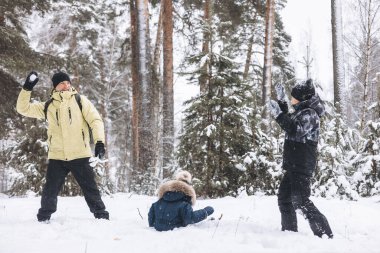 Baba ve oğulları kış ormanında kartopu savaşı yapıyorlar. Dışarıda karda oynayan mutlu çocuklar. Noel tatili, yeni yıl aile tatili. Sıcak giysili kardeşler soğuk günde yürürler.