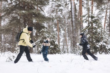 Baba ve oğulları kış ormanında kartopu savaşı yapıyorlar. Dışarıda karda oynayan mutlu çocuklar. Noel tatili, yeni yıl aile tatili. Sıcak giysili kardeşler soğuk günde yürürler.