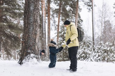 Baba ve oğulları kış ormanında kartopu savaşı yapıyorlar. Dışarıda karda oynayan mutlu çocuklar. Noel tatili, yeni yıl aile tatili. Sıcak giysili kardeşler soğuk günde yürürler.
