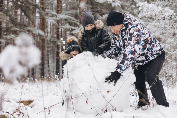 雪深い冬の森の中で雪男のために一緒に大きな雪玉を転がす幸せな父と息子 男喜びのティーンエイジャーと小さな男の子が遊んで家族の散歩を楽しんでいます 冬のアクティビティ — ストック写真