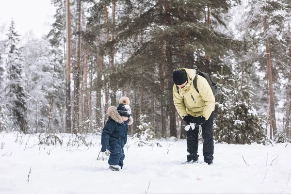 冬の森の中で一緒に雪玉を楽しんでいる父と息子 屋外で雪の中で遊ぶ幸せな子供たち クリスマス休暇 新年の家族の休暇 寒い日に歩く暖かい服の兄弟 — ストック写真