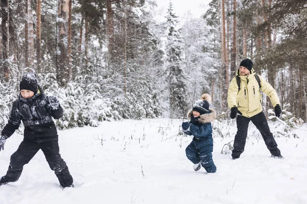 Baba ve oğulları kış ormanında kartopu savaşı yapıyorlar. Dışarıda karda oynayan mutlu çocuklar. Noel tatili, yeni yıl aile tatili. Sıcak giysili kardeşler soğuk günde yürürler.