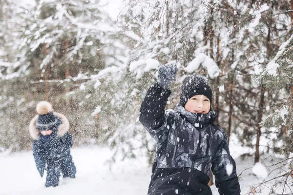 冬の森の雪の上に座って幸せな10代の少年 子供は屋外で楽しんでいます 雪の中で雪の中で遊ぶ楽しい青年 寒い日に冬の公園を歩く笑顔の子供 — ストック写真