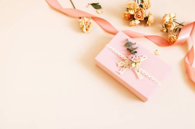 Kuru güller, çiçekler ve pastel arka planda kurdeleler olan güzel pembe hediye kutusu. Tatil hediyesi, doğum günü, düğün, anneler günü, sevgililer günü, kadınlar günü. Uzayı kopyala Üst manzara, düz uzanma