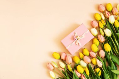 Renkli laleler ve bej renkli pastel arka planda izole edilmiş pembe hediye kutusu. Bahar çiçekleri. Doğum günü için tebrik kartı, kadın, anneler günü, sevgililer günü. Düz yatıyordu. Boşluğu kopyala.