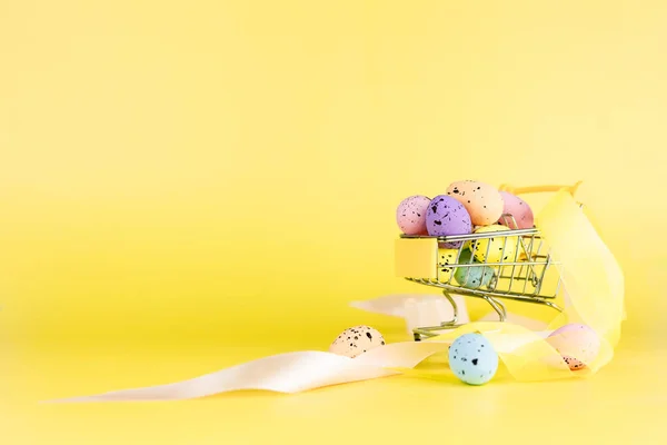 黄色の背景にショッピングカートでカラフルなイースターウズラの卵 コピースペース ミニマルイースターのコンセプト — ストック写真
