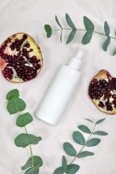 white packaging for lotion on a white background surrounded by a pomegranate and a dry flower and a green creeper