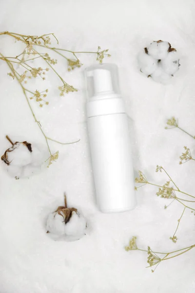 white packaging for lotion on a white background surrounded by cotton and dry flower