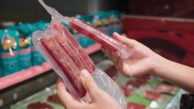 Süpermarkette el ele tutulan vakum paketlerinde iki paket organik et sosislerini karşılaştırmak.